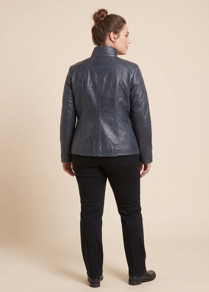 A woman shown from the back wearing a dark slate blue leather jacket, black pants, and black shoes against a solid beige studio background.