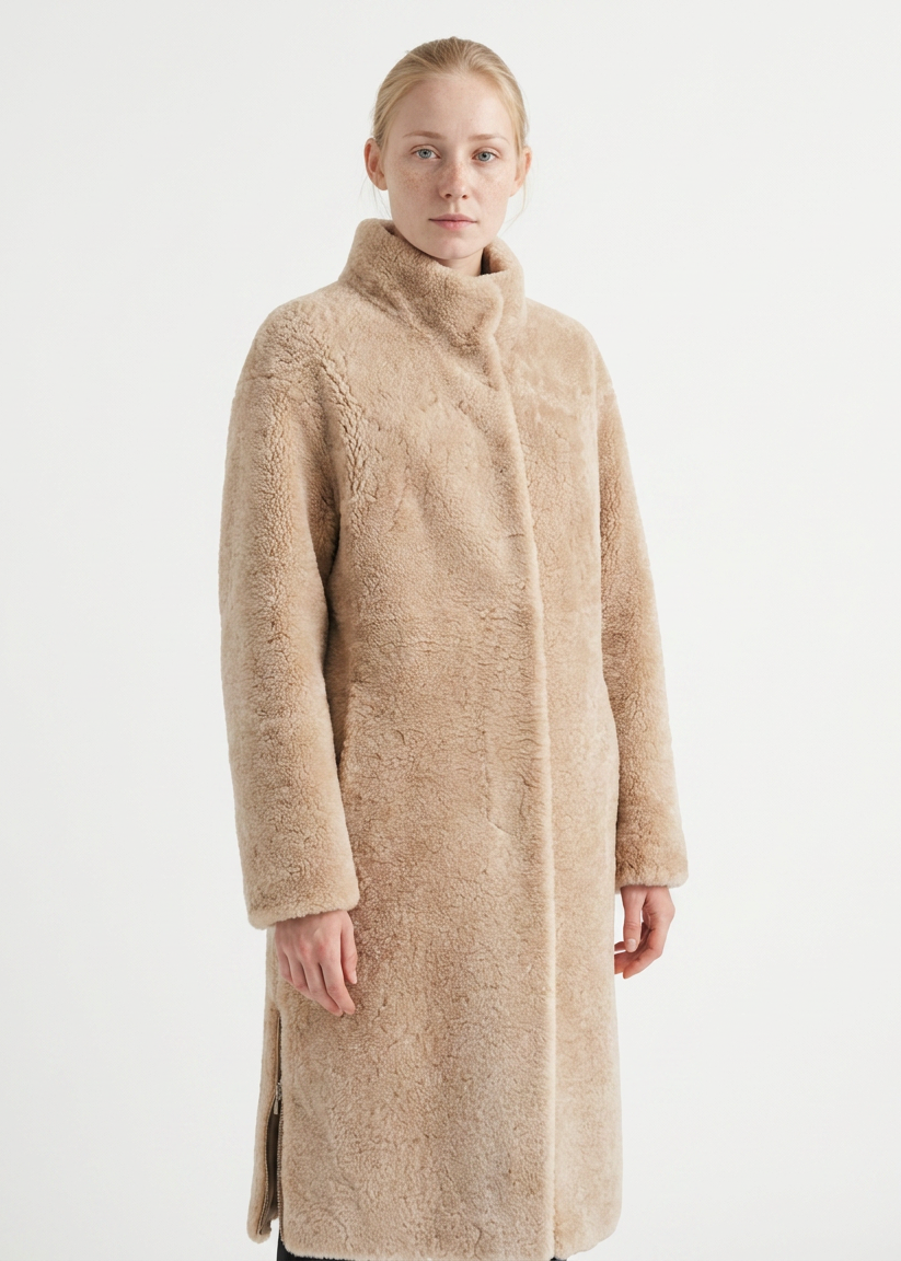 A woman wearing a long, high-neck teddy coat in a light beige color, photographed against a plain white studio background.